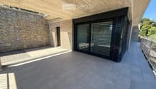 Modern balcony with concrete ceiling, tiled floor, stone wall, and large sliding glass door.