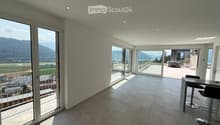 Modern, open-plan room with large glass doors leading to a balcony, tiled floor, bar counter with two stools, and scenic mountain view.