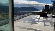 Modern balcony with large glass doors, tiled floor, metal railing, and scenic mountain and lake view.
