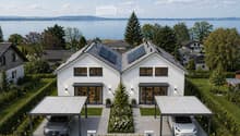 Modern two-story house with white exterior, large windows, solar panels on the roof, and a landscaped garden with a view of a lake.