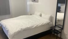 A modern bedroom with a neatly made bed, a large mirror, a nightstand, and a picture frame on the wall.