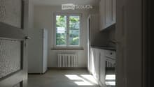 Empty kitchen with white cabinets, a window, a radiator, and a refrigerator. No furniture or appliances are present.