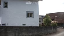 White plastered wall, brown roof, grey concrete fence, two windows, a window on the corner