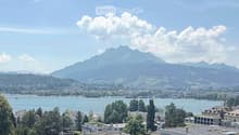 Panoramic view of a cityscape with a lake, mountains, and scattered buildings.