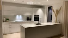 Modern kitchen with white cabinetry, a central island, and marble countertops. Features include a sink with a modern faucet, an oven, and decorative elements like a plant and a vase with dried flowers.