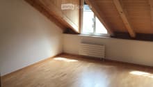 Empty attic room with wooden floor, exposed wooden beams, and a single window letting in natural light.