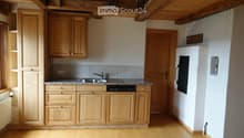 Compact kitchen with light wooden cabinets, granite countertop, sink, dishwasher, and refrigerator. Wooden floor and exposed wooden beams on the ceiling.