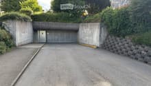 A concrete garage entrance with a raised ground floor, surrounded by greenery and a stone wall.