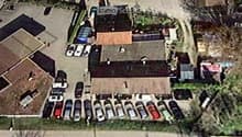 Aerial view of a multi-building complex with parking lot, several structures, and surrounding greenery.