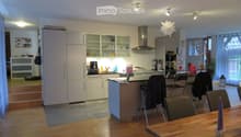 Modern kitchen with white cabinets, stainless steel appliances, island, and dining area with wooden table and chairs.