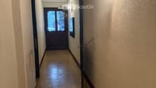 Hallway with beige tiled floor, light-colored walls, and a decorative door at the end.