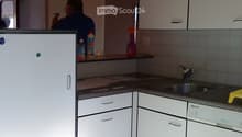 modern kitchen with white tiles, cabinets, countertop, sink, dishwasher, bottles, yellow sponge, wooden beam