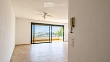 Empty hallway with tiled floor, white walls, ceiling fan, and large sliding glass door leading to a balcony with a scenic view.