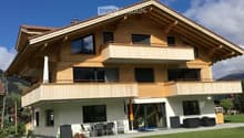 Two-story house with wooden balconies, large windows, and a well-maintained lawn.
