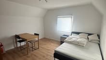 Bedroom with wooden flooring, a bed with white bedding, a nightstand, a small table, and chairs.