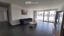 Modern living room with dark tiled flooring, grey sofa, glass coffee table, TV stand, and large sliding glass doors leading to a balcony.