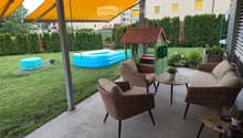 Balcony with wicker furniture, including a sofa, chairs, and small tables, with a view of a backyard featuring a playhouse, inflatable pool, and greenery.