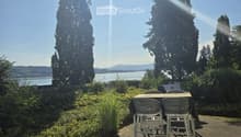 Outdoor patio with a table and chairs, overlooking a scenic lake and tall trees.