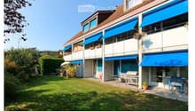 A multi-story residential building with blue awnings, balconies, and a well-maintained lawn in front.