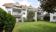 A modern two-story house with white exterior, red-tiled roof, multiple balconies, and a well-maintained lawn in front.