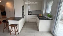 Modern kitchen with white cabinets, black countertops, a central island with two stools, a sink with a faucet, and a coffee machine on the counter.