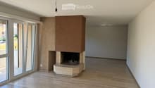 Empty room with wooden flooring, white walls, large glass doors, and a built-in fireplace with a stone base and wooden mantel.