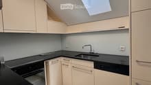 Modern kitchen with white cabinets, black countertops, and built-in appliances including a sink, oven, and dishwasher. Features a skylight window and sleek design.