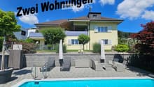 Yellow house, brick wall, blue pool, patio with lounge chairs and tables, fence, trees and plants