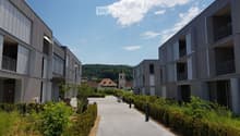Modern residential complex with grey facades, balconies, and a landscaped courtyard with pathways and greenery.