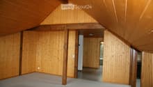 Empty attic space with wooden walls, exposed wooden beams, and a carpeted floor. No furniture or equipment is present.