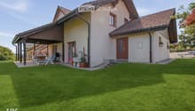 Two-story house with beige walls, red-tiled roof, and a covered patio area with outdoor furniture.