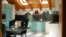 Wooden ceiling, wooden floor, green cupboards, white kitchen table, black chairs, countertop, kitchen appliances, wall mounted lamps