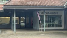 Two-story building with a tiled roof, a covered entrance area, and signage reading "Foto Fachgeschäft" (photo shop).