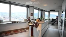 Modern kitchen with large windows offering a scenic view, featuring a kitchen island, cabinets, a sink, a stool, a chair, and a framed picture on the wall.