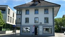 A three-story building with a classic European architectural style, featuring a tiled roof, multiple windows, and a storefront with signage reading "farm2kasse" and a RE/MAX logo.