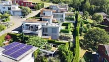 Aerial view of a residential neighborhood with multiple modern houses, well-maintained gardens, and solar panels on one roof.