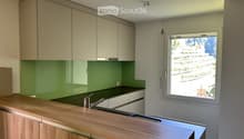 Modern kitchen with light-colored cabinets, green backsplash, wooden countertop, and stainless steel sink.