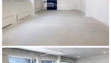 Empty room with concrete floor, white walls, large windows, and a blue door.