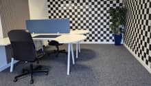 Modern office space with white desks, black office chairs, a computer screen, and a potted plant. The walls feature a black and white checkered pattern.