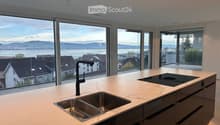 Modern kitchen with a marble countertop, stainless steel sink, black faucet, and induction cooktop, large windows offering a scenic view of the city and water.