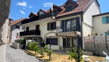 Two-story house with white exterior, multiple balconies, and a small garden area with chairs and a table.