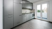 Modern kitchen with dark gray cabinets, light gray countertops, silver sink, stainless steel faucet, large windows, balcony
