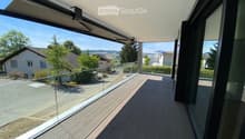 Modern balcony with wooden decking, glass railing, and scenic view of surrounding houses and landscape.