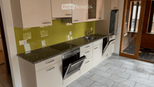 Modern kitchen with light-colored cabinets, granite countertop, stainless steel appliances, and a green backsplash.