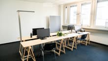 Modern office space with multiple desks, chairs, computer screens, keyboards, and a small plant on one of the desks.