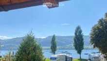 View of a lakeside area with several RVs parked near the water, surrounded by trees and a clear blue sky.
