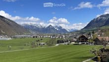 Scenic view of a town nestled in a valley surrounded by mountains, with green fields and scattered buildings.