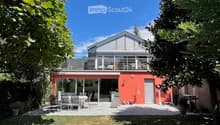 Modern orange house with a large balcony and outdoor dining area, surrounded by greenery and trees.