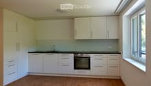 Modern kitchen with white cabinets, wooden flooring, and built-in appliances including a sink, faucet, and oven.