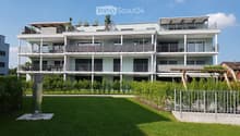 Multi-story apartment building with modern design, large balconies on each floor, green garden area in front, well-maintained surroundings.